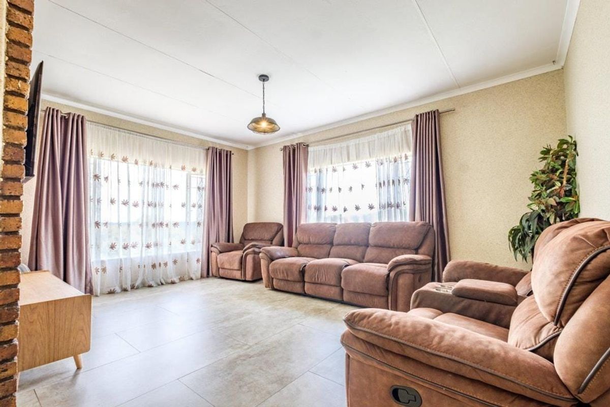 A spacious living room featuring tiled flooring, an exposed brick feature wall, and large windows allowing for ample natural light.