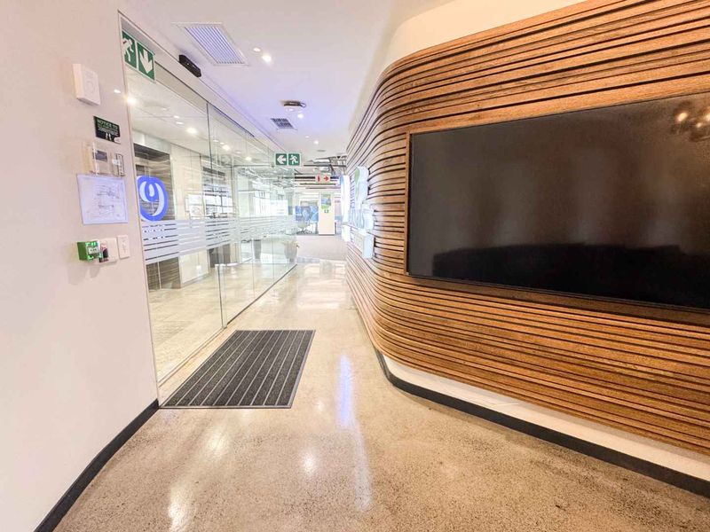 Modern office hallway featuring polished concrete floors, a curved timber slat feature wall, and glass partitions leading into the workspace.