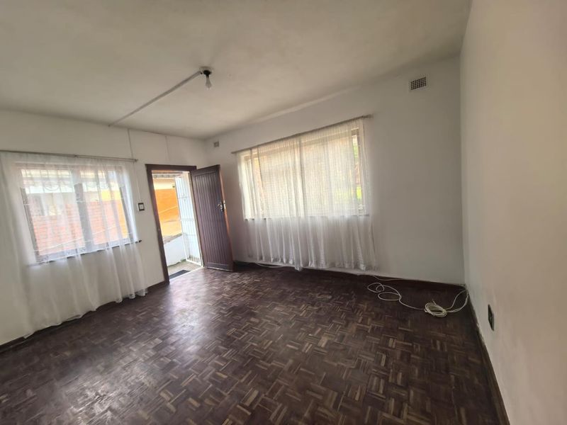 An empty living room featuring original parquet flooring, large windows with natural light, and direct access to an exterior area.