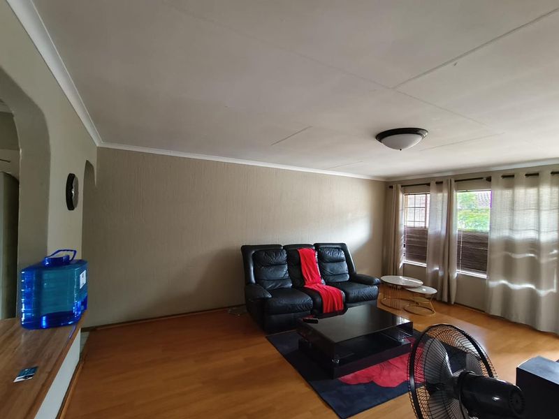 A living room featuring laminate flooring, coved ceilings, and large windows with fitted blinds, providing a functional and neutral living space.