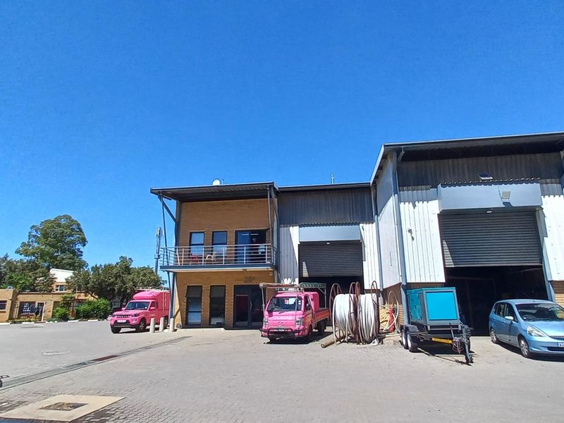 Front elevation of an industrial property featuring facebrick and metal cladding, roller shutter doors, and a paved yard area.