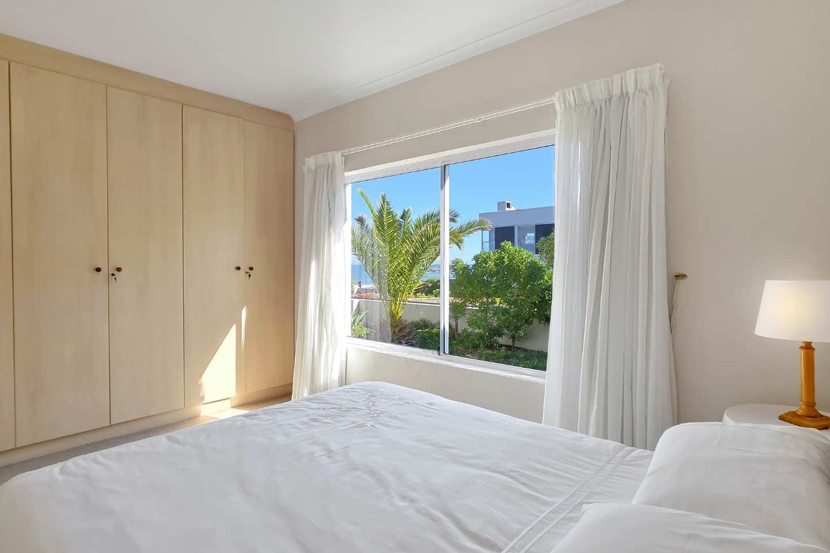 Bright bedroom featuring built-in light wood cabinetry and a large window offering pleasant garden and coastal views.