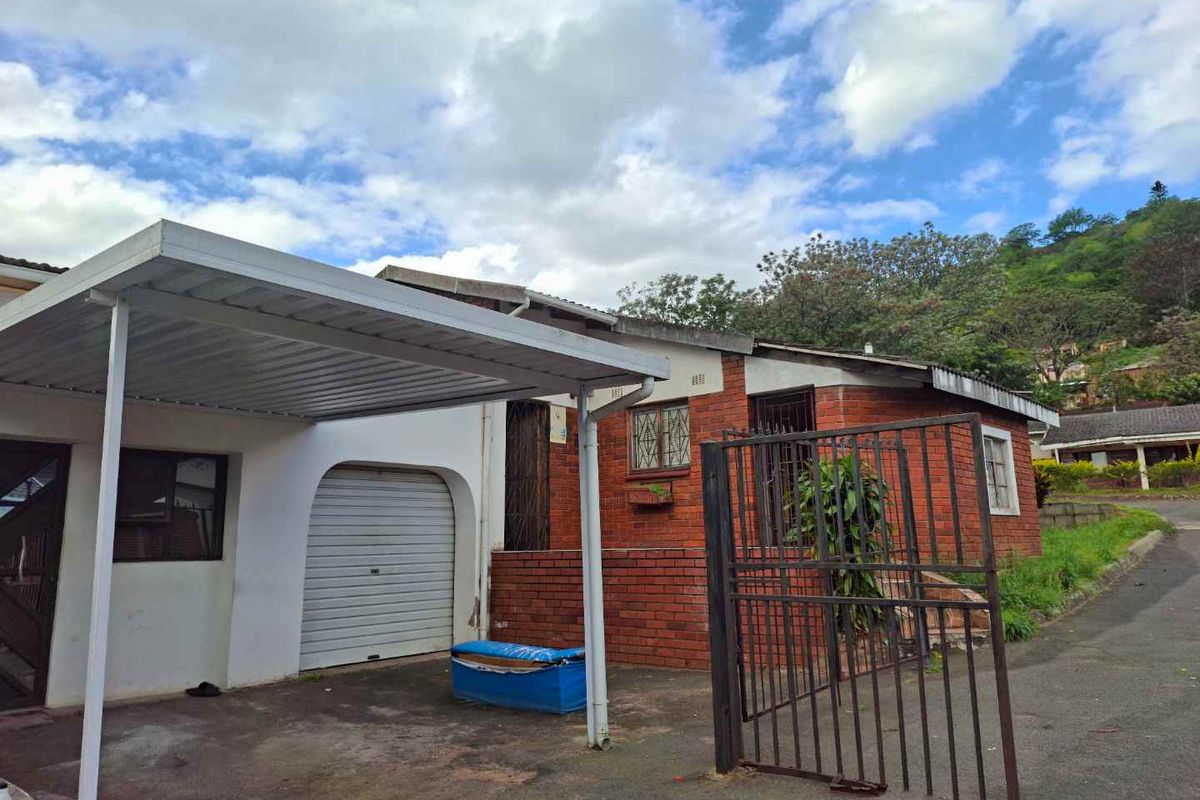 Front exterior view of a townhouse featuring a carport, roller garage door, and brick facade with security features.