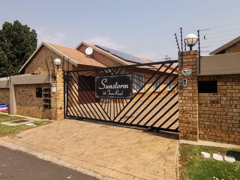 Front entrance view of a cluster property featuring a brick facade, secure sliding gate, electric fencing, and solar panels installed on the tiled roof.