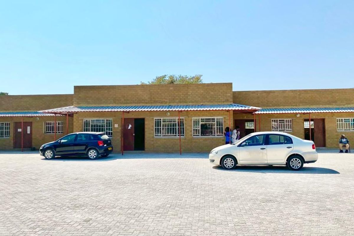 Front exterior view of a single-story commercial building featuring a paved parking area, covered walkway, and brick facade with security-barred windows.