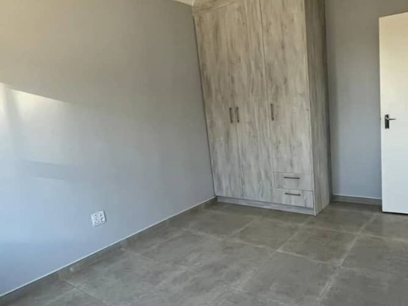 A clean, empty bedroom featuring neutral grey walls, large format floor tiles, and a modern built-in wardrobe with wood-grain finish.