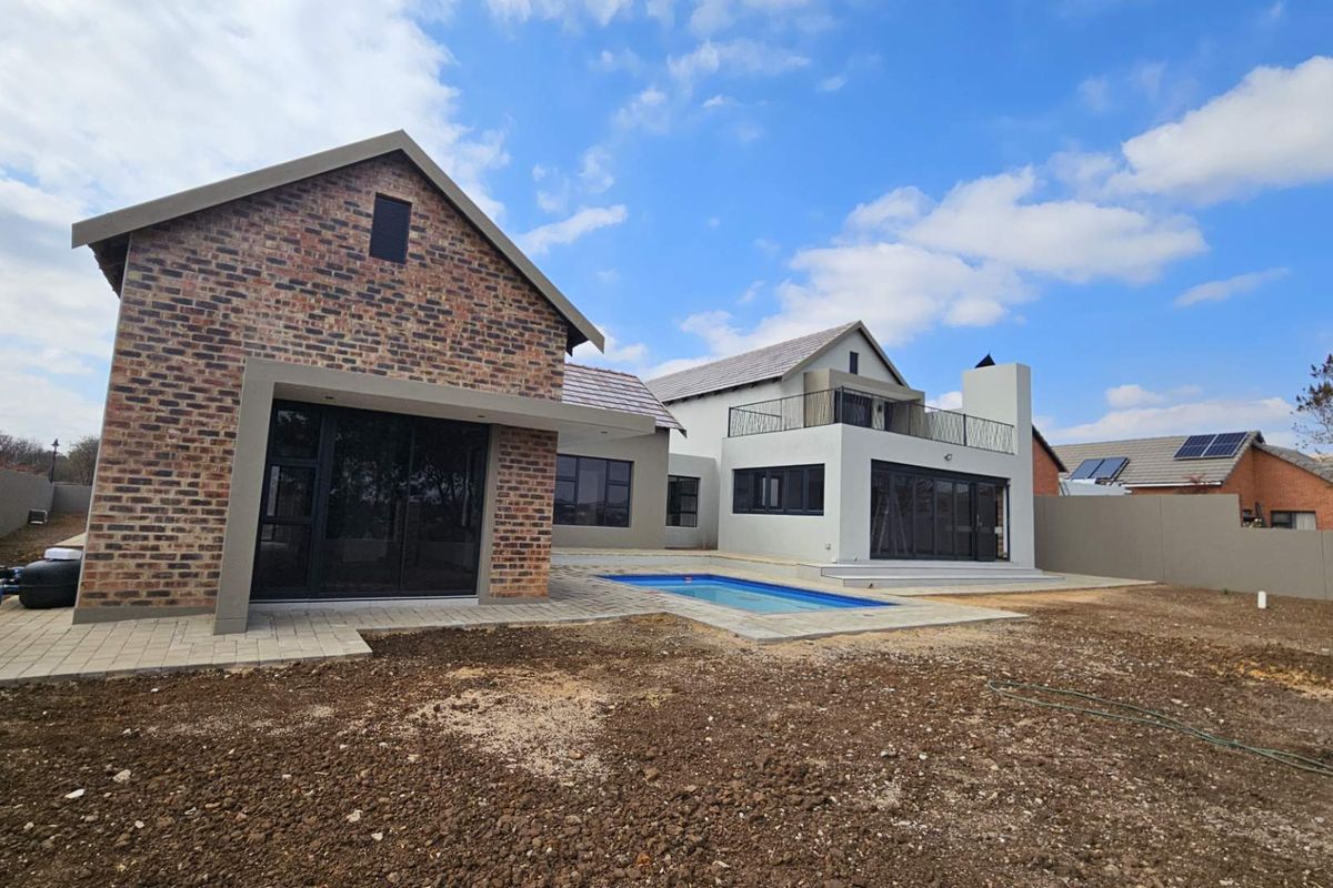 Rear view of a modern double-story house featuring a swimming pool, brick and plaster facade, and large sliding glass doors leading to the patio.
