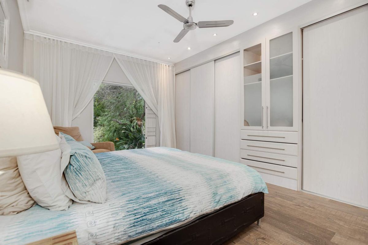 A bright bedroom featuring built-in floor-to-ceiling wardrobes with integrated shelving and drawers, wood-look flooring, and a ceiling fan.