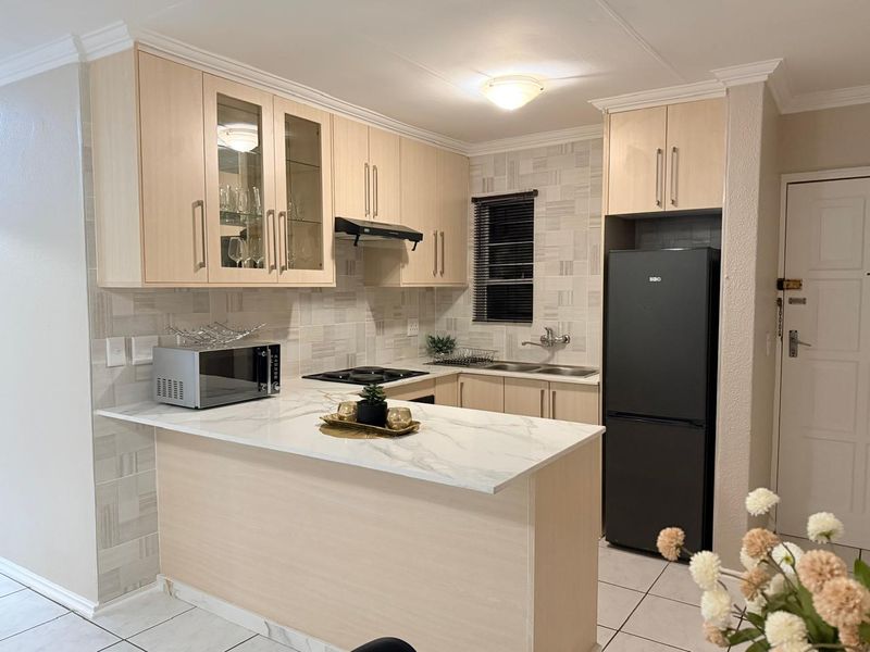 Modern kitchen featuring light wood cabinetry, marble-look countertops, a breakfast bar, tiled backsplash, and integrated hob with extractor fan.