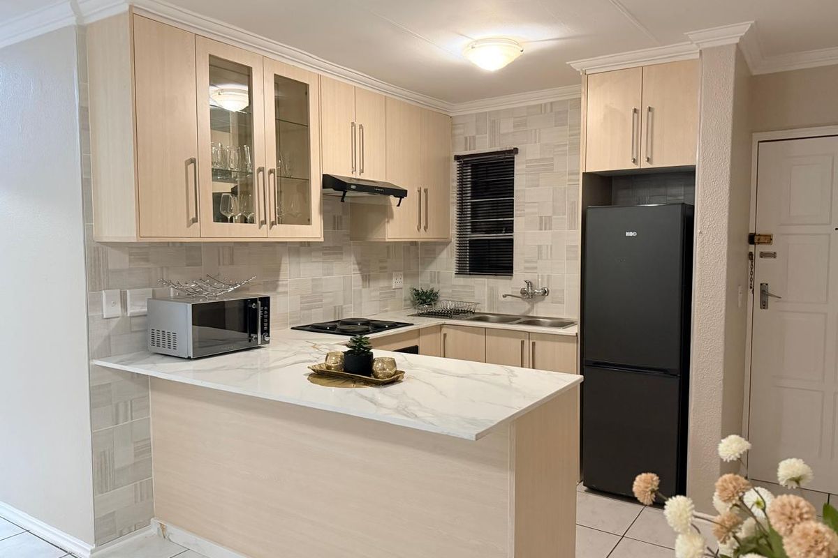 Modern kitchen featuring light wood cabinetry, marble-look countertops, a breakfast bar, tiled backsplash, and integrated hob with extractor fan.