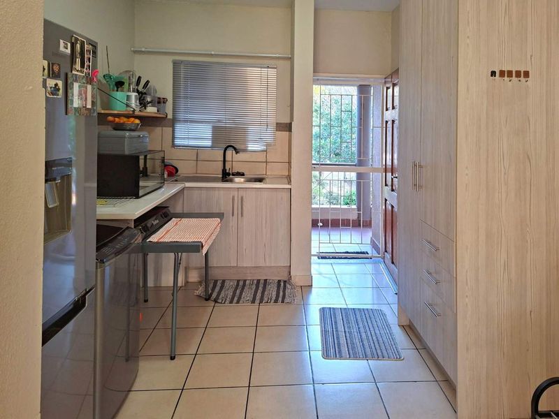 Compact kitchen featuring light wood-finish cabinetry, tiled flooring, and direct access to an outdoor area through a security gate.