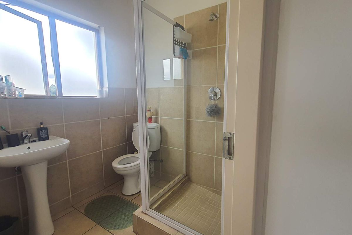 A functional bathroom featuring a pedestal basin, a toilet, and a glass-enclosed shower with neutral wall and floor tiling.