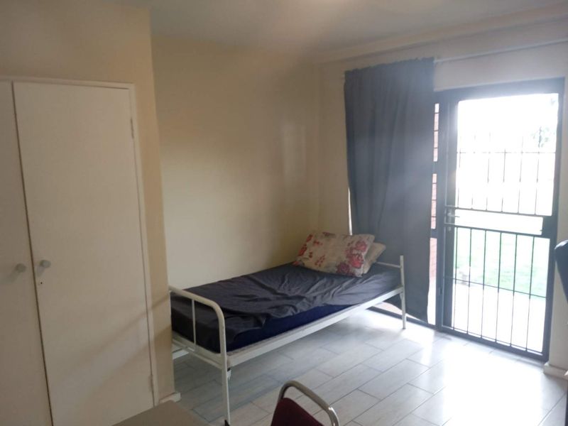 A functional bedroom featuring tiled flooring, a built-in wardrobe, and direct access to the outdoors through a secure sliding glass door.