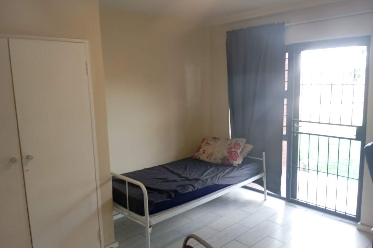 A functional bedroom featuring tiled flooring, a built-in wardrobe, and direct access to the outdoors through a secure sliding glass door.