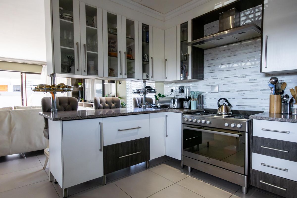 Modern kitchen featuring white and dark wood cabinetry, stone countertops, a gas stove with extractor fan, and a stylish tiled backsplash.