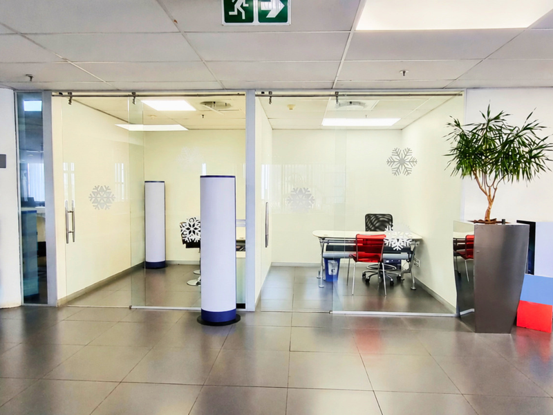 Modern office space featuring glass-partitioned private offices, suspended ceilings with recessed lighting, and durable tiled flooring in a professional commercial setting.