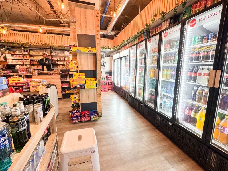 Interior view of a retail convenience store featuring multiple commercial glass-door refrigeration units, service counter, and industrial-style exposed ceiling.