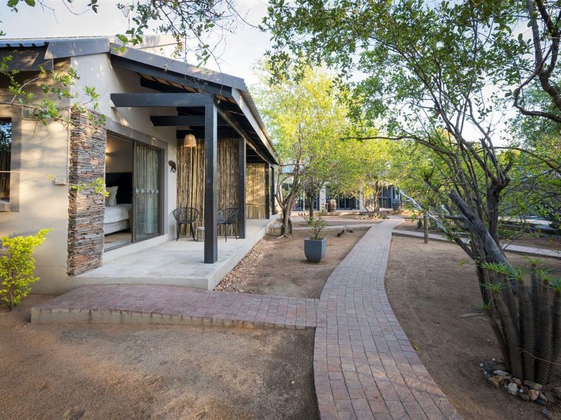 A well-maintained guest house exterior featuring a covered patio, stone-clad accents, and a brick-paved walkway leading through a landscaped garden area.