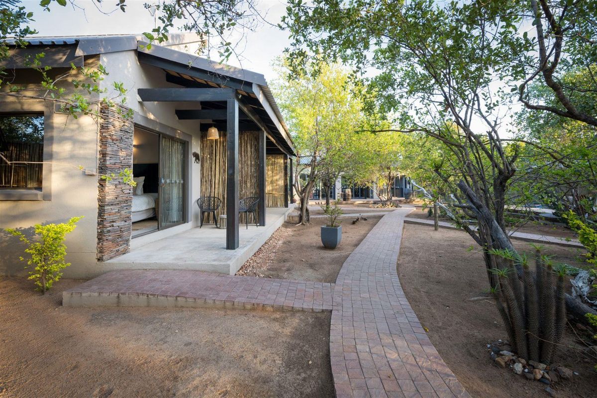 A well-maintained guest house exterior featuring a covered patio, stone-clad accents, and a brick-paved walkway leading through a landscaped garden area.
