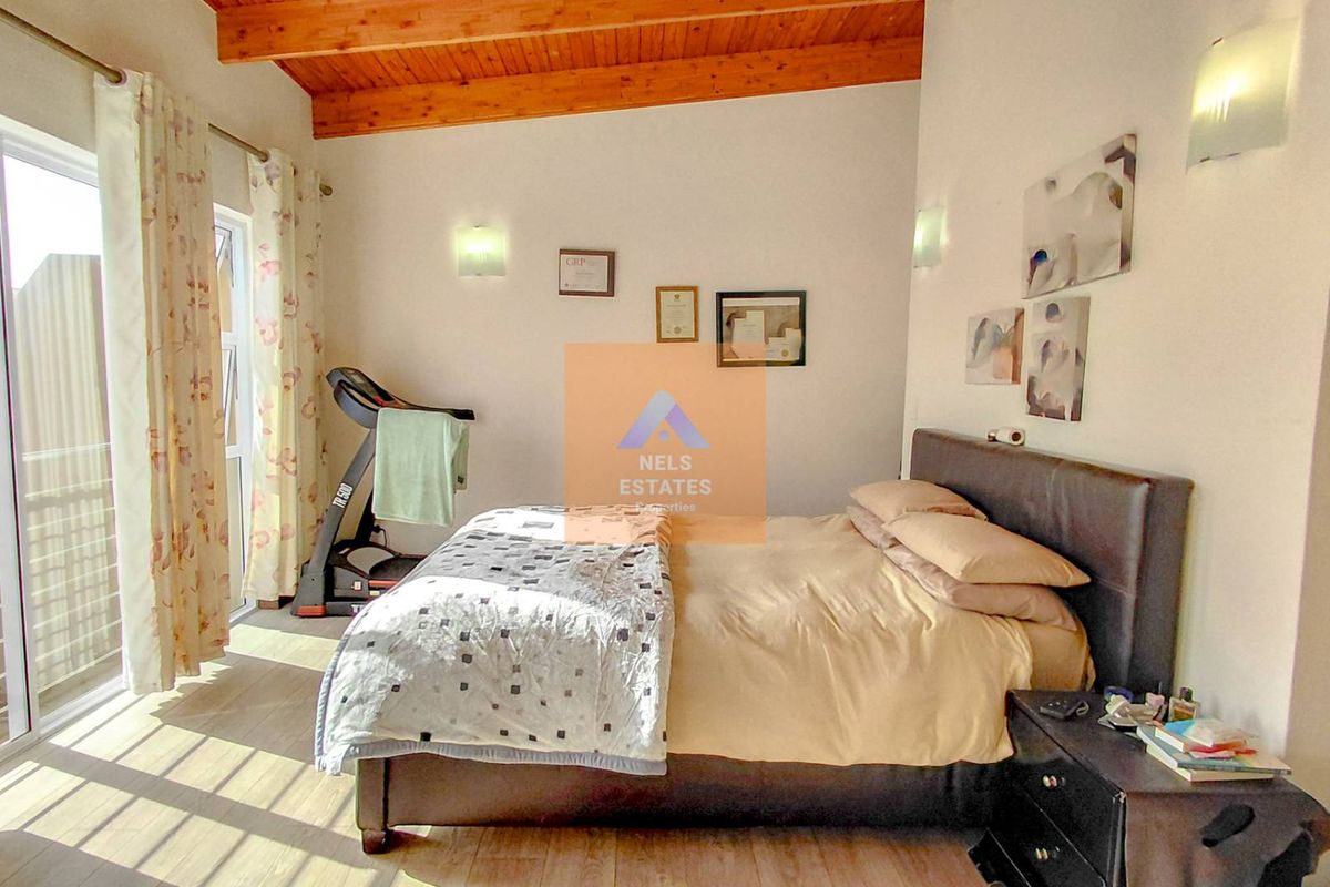 A bedroom featuring high vaulted timber ceilings, laminate flooring, and sliding glass doors providing access to an outdoor area.