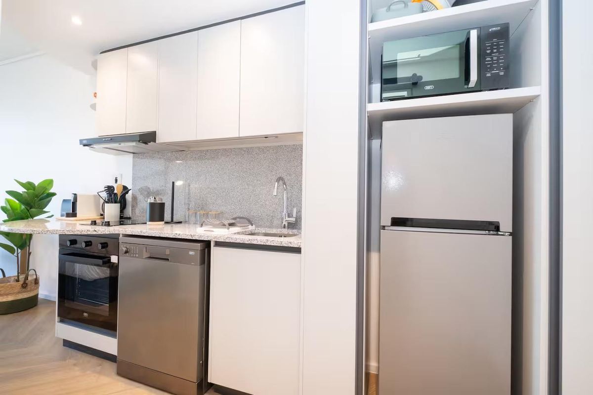 Modern kitchen featuring sleek white cabinetry, granite countertops, stainless steel appliances, and a dedicated built-in microwave shelf.