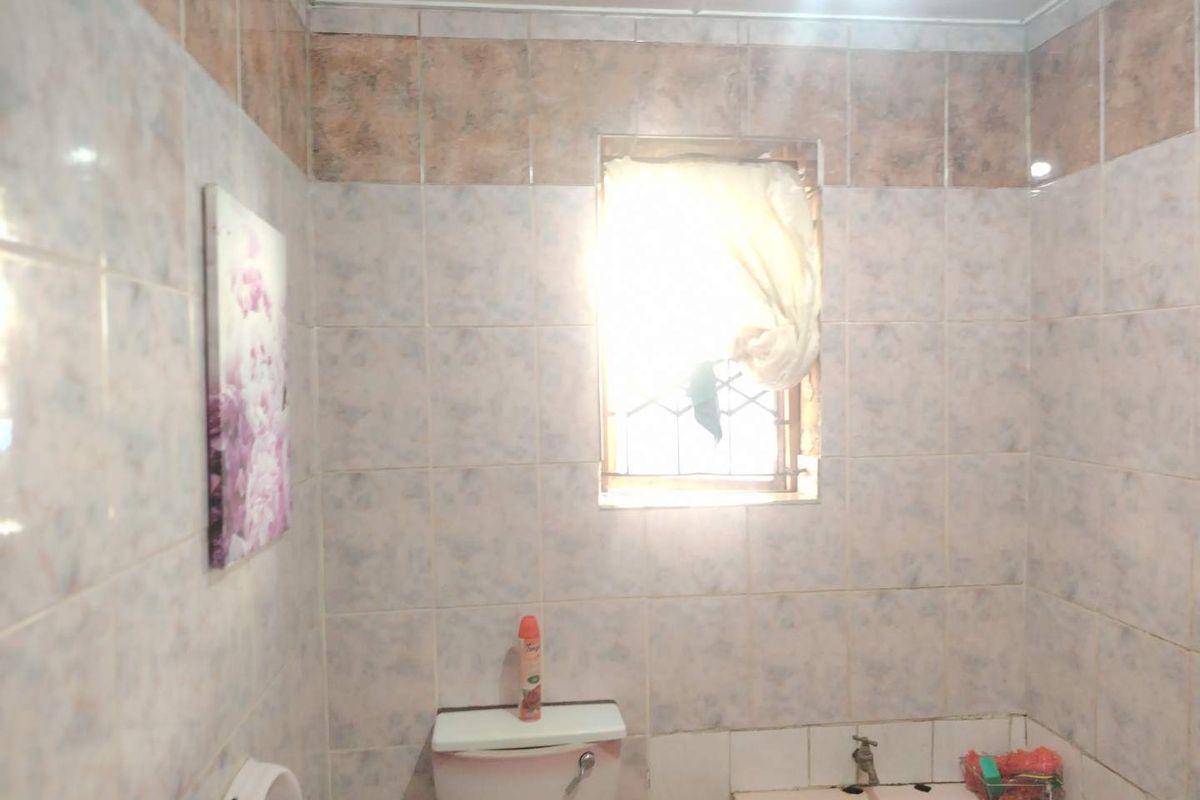 A dated bathroom featuring ceramic wall tiles, a built-in bathtub, and a toilet, requiring modernization to improve its aesthetic appeal and functionality.