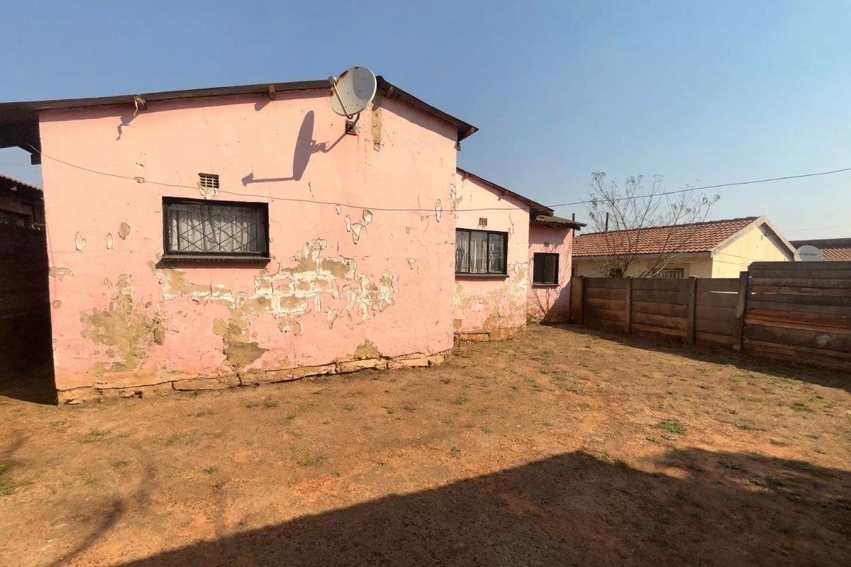 Rear view of the property showing a garden area and the exterior wall with significant paint peeling and masonry exposure.