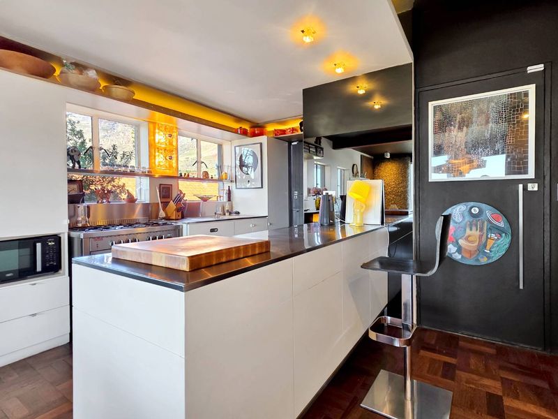 Modern kitchen featuring a large stainless steel island, built-in gas hob, sleek cabinetry, and warm recessed lighting, set against dark accent walls and parquet flooring.
