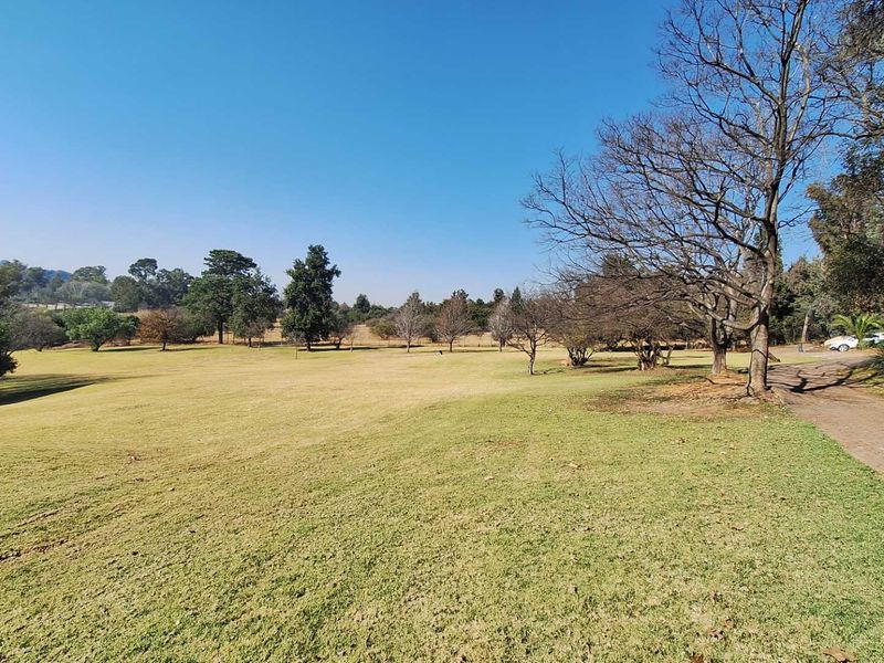 A spacious, well-maintained garden area featuring a large lawn, mature trees, and a paved driveway leading through the property grounds.