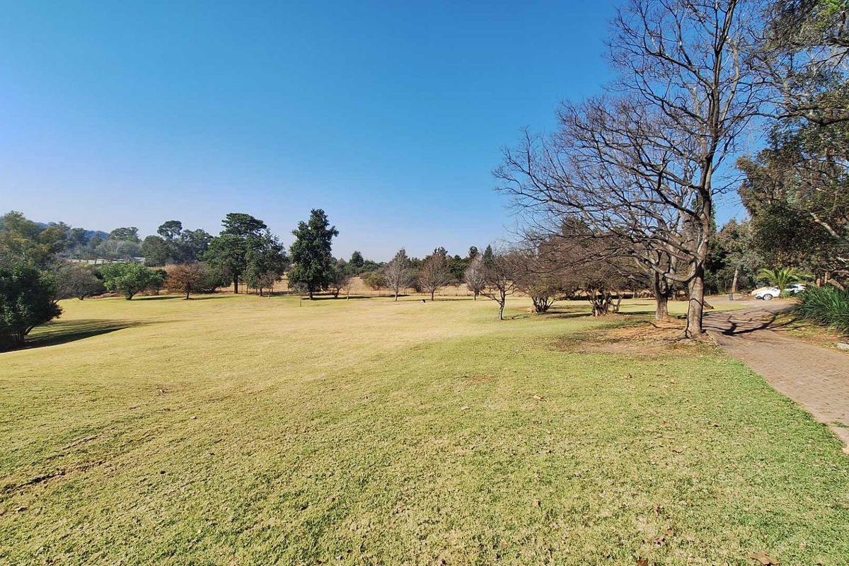 A spacious, well-maintained garden area featuring a large lawn, mature trees, and a paved driveway leading through the property grounds.