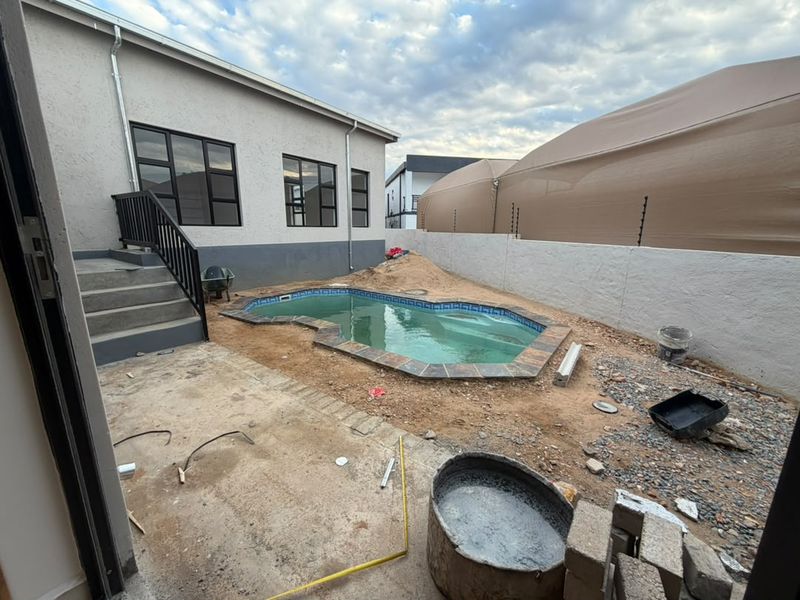 Rear exterior view featuring a swimming pool with surrounding unfinished landscaping and construction debris, requiring completion to enhance the outdoor living space.
