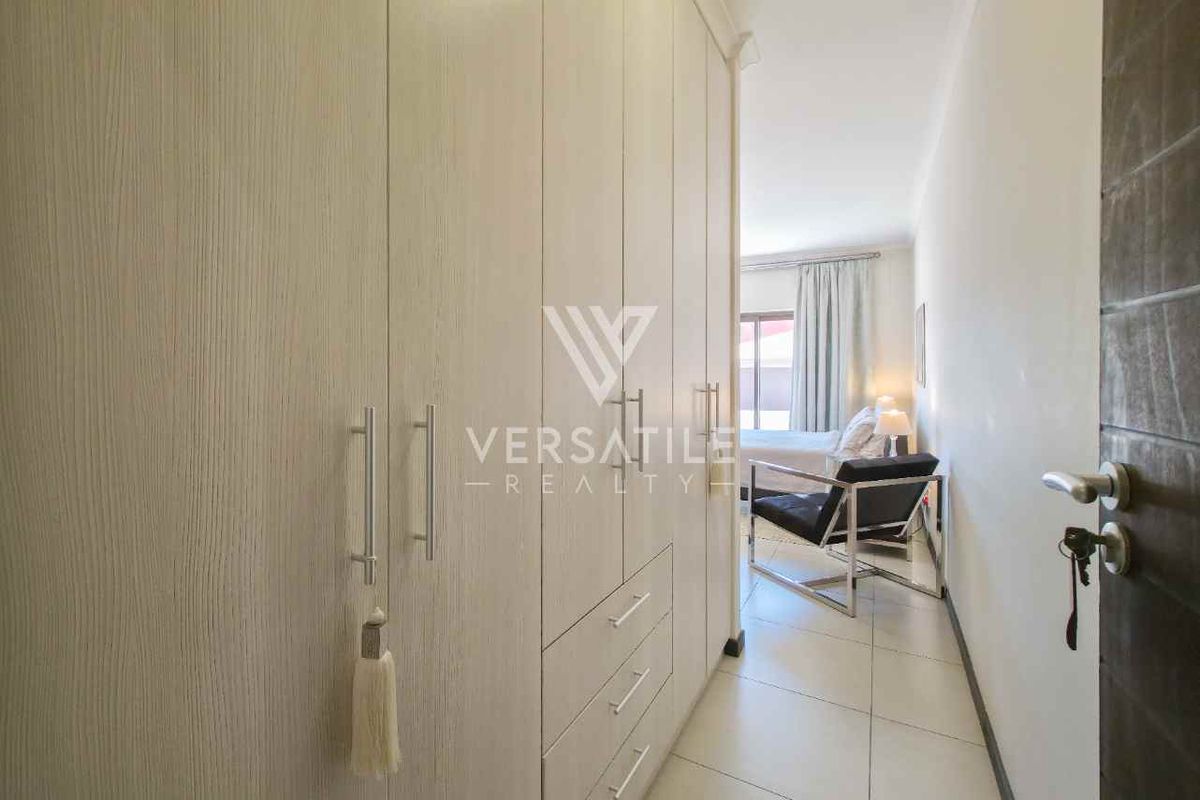 A bedroom featuring extensive built-in cupboards with light wood-grain finish and neutral floor tiles.
