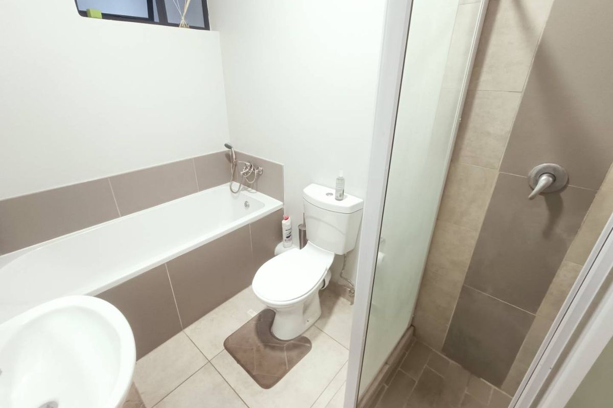 A functional bathroom featuring a built-in bathtub, a separate glass-enclosed shower, a toilet, and a pedestal sink with neutral wall and floor tiling.