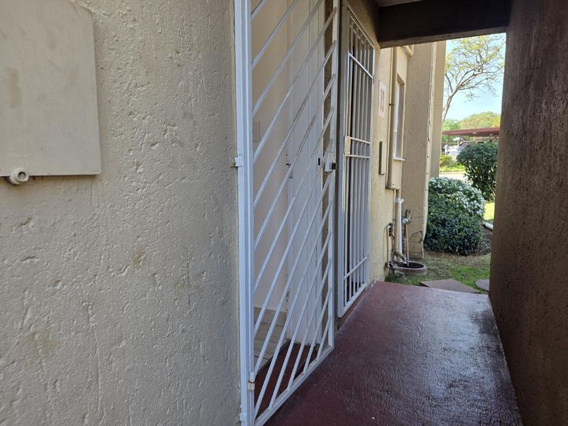 Exterior entrance area featuring a security gate, textured wall finish, and a painted concrete walkway leading to the apartment door.