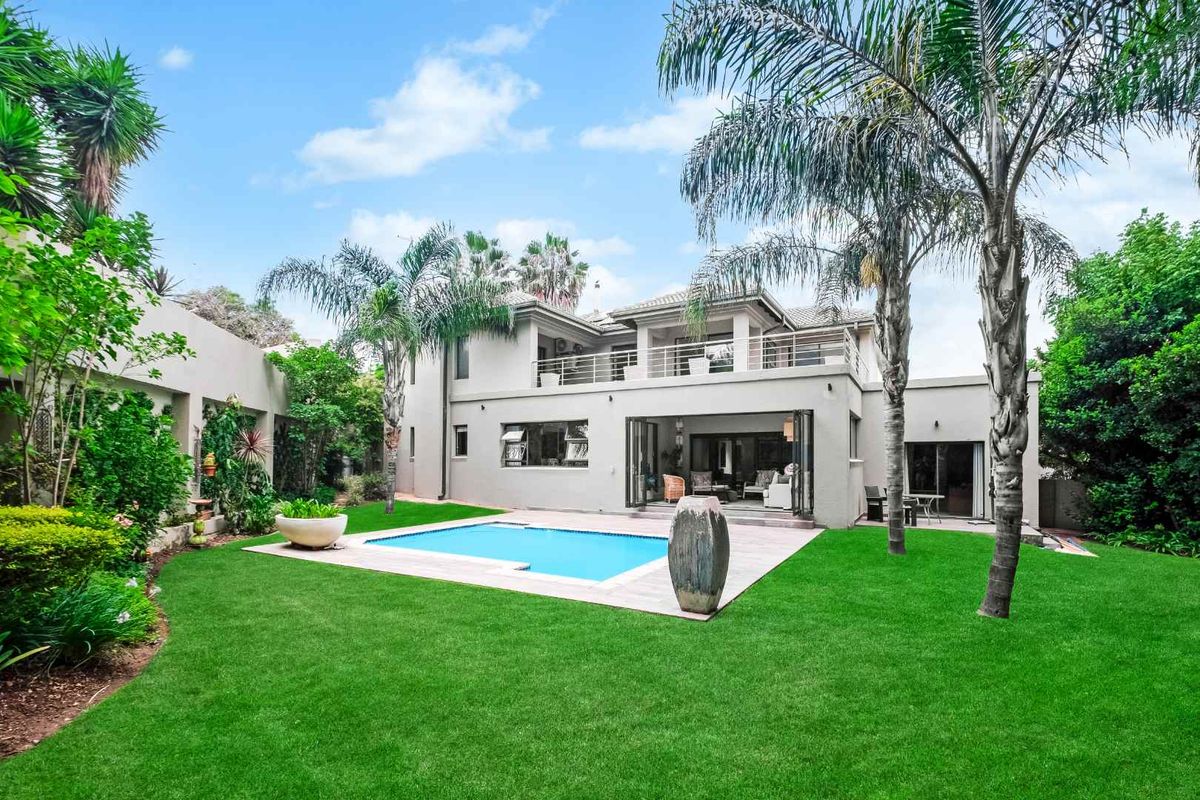Rear view of a two-story residence featuring a swimming pool, landscaped garden, and a covered patio area with large folding glass doors.