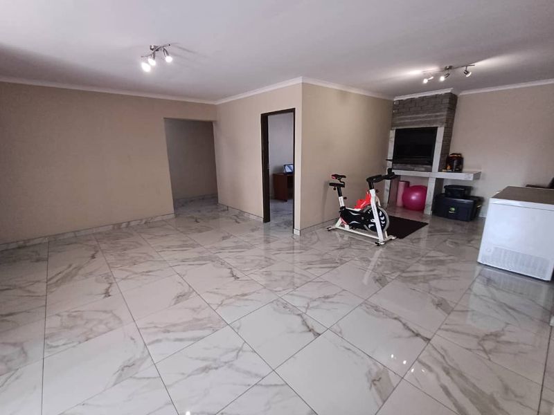 Spacious living area featuring large-format marble-look porcelain floor tiles and a built-in brick fireplace, offering a versatile open-plan layout.