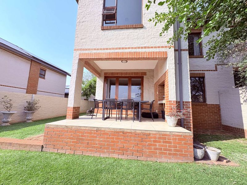 A rear view of the townhouse featuring a covered patio with a built-in braai, brick detailing, and access to the garden.
