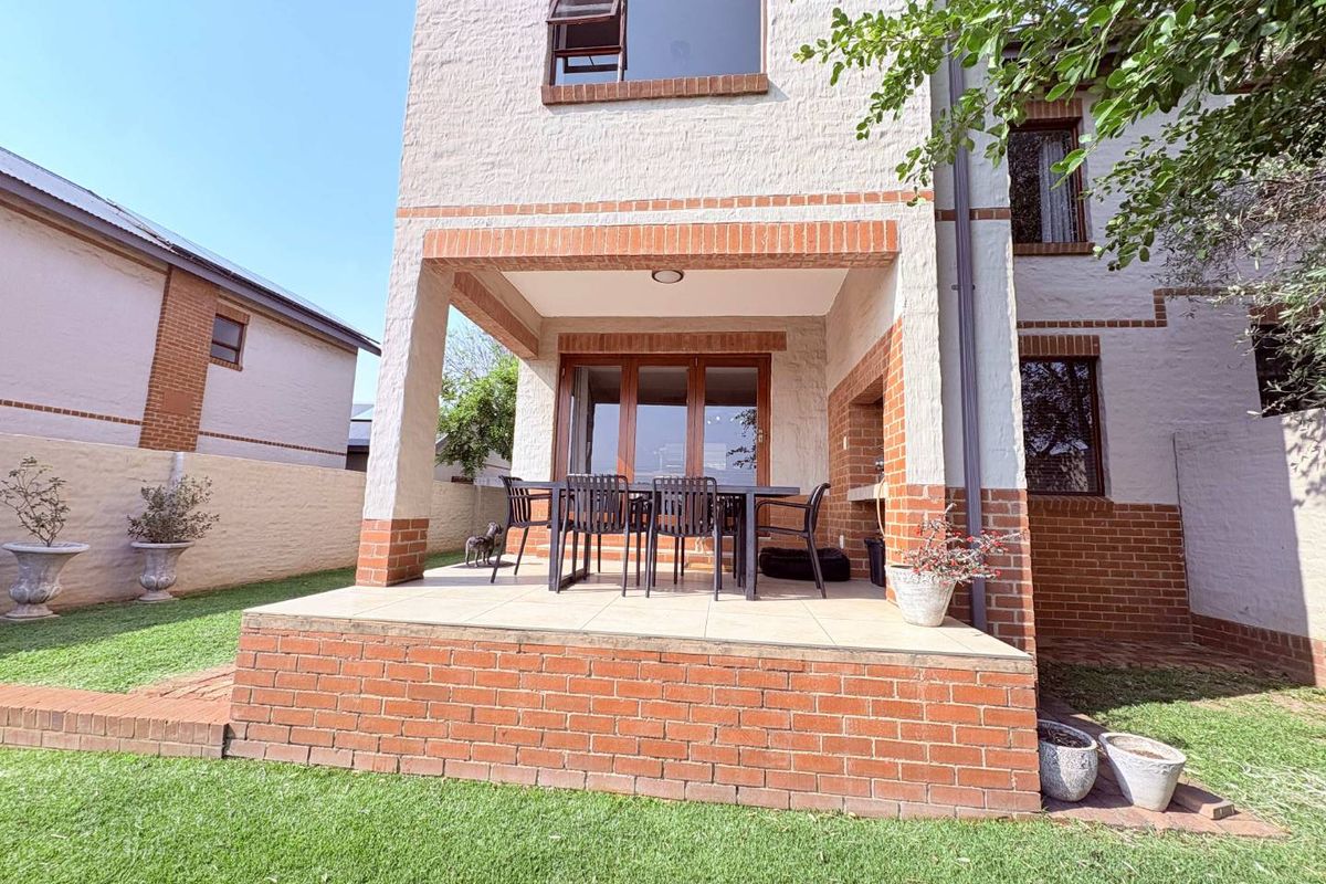 A rear view of the townhouse featuring a covered patio with a built-in braai, brick detailing, and access to the garden.