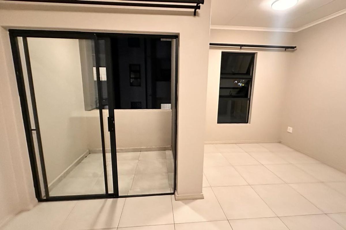 A bright, empty living area featuring neutral tiled flooring, modern black-framed windows, and a sliding glass door leading to a private balcony.