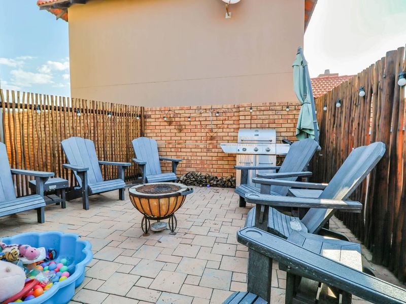 A paved outdoor patio area featuring a brick boundary wall, timber pole fencing, and a built-in gas braai for outdoor entertaining.