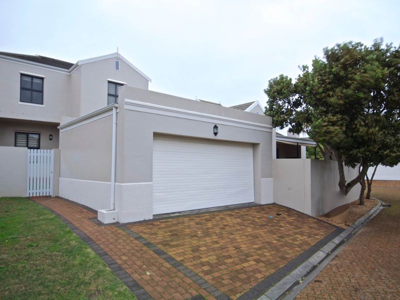 Front exterior view of the townhouse featuring a single garage, paved driveway, and secure pedestrian gate access.
