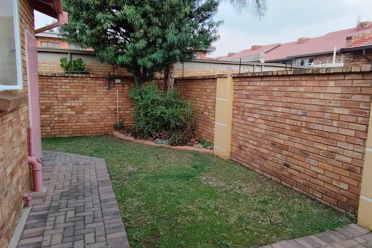 A private rear garden area featuring a paved walkway, established perimeter brick walling, and a small lawn section.