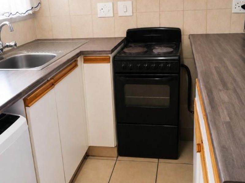 A functional kitchen featuring laminate countertops, built-in cabinetry, a stainless steel sink, and a freestanding electric stove with tiled backsplash and flooring.