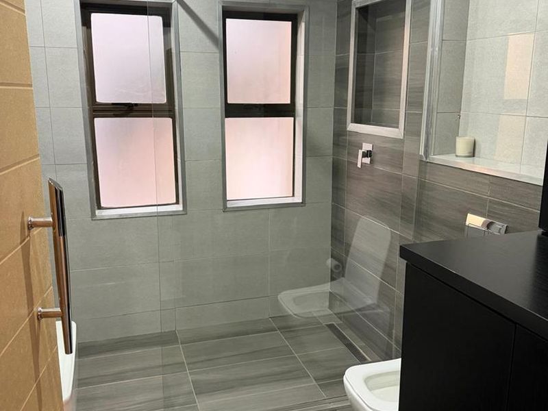 Modern bathroom featuring a walk-in shower with a glass screen, rain shower head, wall-hung toilet, and contemporary grey tiled finishes.