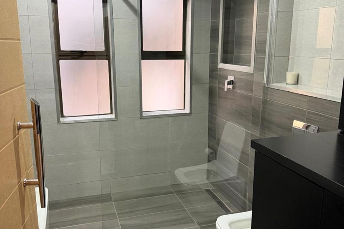 Modern bathroom featuring a walk-in shower with a glass screen, rain shower head, wall-hung toilet, and contemporary grey tiled finishes.