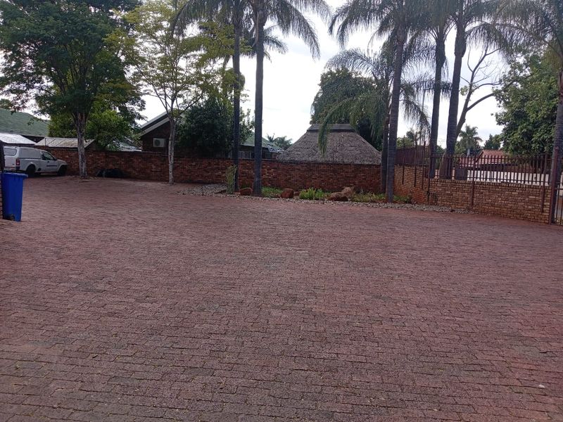 A spacious paved driveway area featuring a brick boundary wall and mature palm trees, providing ample parking space.