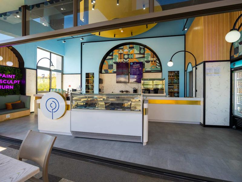Modern commercial service area featuring a refrigerated display counter, integrated shelving, and vibrant blue wall accents with large sliding glass doors.