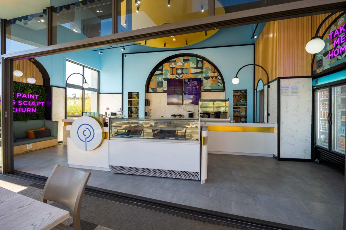 Modern commercial service area featuring a refrigerated display counter, integrated shelving, and vibrant blue wall accents with large sliding glass doors.