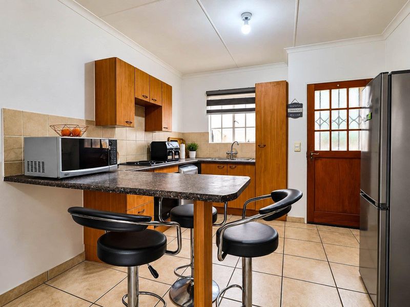 A functional kitchen featuring laminate cabinetry, tiled backsplash, ceramic flooring, and a breakfast bar, with direct access to the exterior.