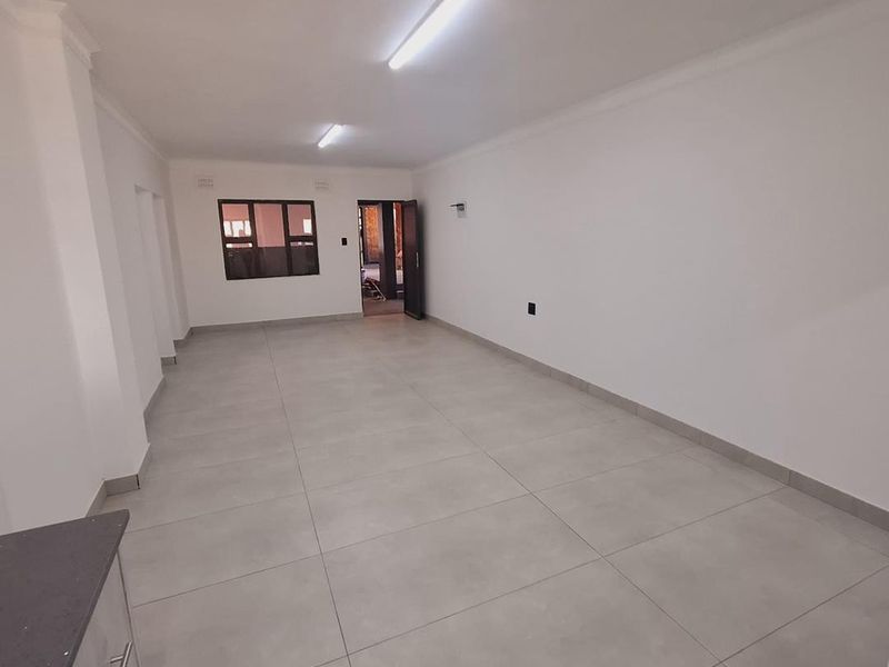 Spacious open-plan living area featuring neutral large-format floor tiles, clean white walls, and modern aluminium window frames.
